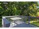 View of a gray wooden deck with a metal table and railing overlooking the lush green trees at 4505 Woodlawn Dr, Raleigh, NC 27616