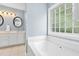 Bright bathroom featuring a garden tub, tile flooring, vanity with oval mirror, and blue walls at 8513 Buscot Ct, Raleigh, NC 27615