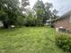 Spacious backyard with mature trees, grass lawn and rear view of brick home with HVAC units at 503 Adams St, Henderson, NC 27536