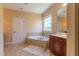 Corner bathtub, window with backyard view, vanity, and neutral tile flooring at 9701 Corktree Ct, Wake Forest, NC 27587