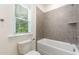 Well-lit bathroom featuring a gray tile shower/tub combo and a window for natural light at 1417 Westmoreland Dr, Raleigh, NC 27612