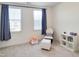 Bedroom featuring windows with blue curtains, neutral carpet, rocking chair, and storage shelving at 1425 Sierra Glen Cir, Apex, NC 27502