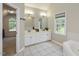 Bright bathroom featuring a double sink vanity, tile flooring, soaking tub and a view of the landscaped yard at 1005 Fairfax Woods Dr, Apex, NC 27502