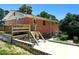 Back of brick home with a wooden deck, concrete patio, and driveway surrounded by lush greenery at 3323 Baugh St, Raleigh, NC 27604