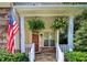 Inviting covered front porch with stone flooring, hanging ferns, white railings, and an American flag at 1437 Lindenberg Sq, Wake Forest, NC 27587