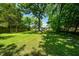A sunny, sprawling backyard with mature trees provides ample shade and space to enjoy the outdoors at 313 13Th St, Butner, NC 27509