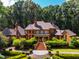 Aerial view showcases the brick home's grand design and manicured landscaping, backing onto wooded area at 8200 Bromley Rd, Hillsborough, NC 27278