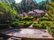Exterior view featuring a brick home and geometric hedges surrounding a patio, backing onto a wooded area at 8200 Bromley Rd, Hillsborough, NC 27278