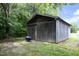 Wooden outbuilding with sliding doors and a blue wheelbarrow in front, surrounded by lush greenery at 4345 Mcintyre Rd, Gibsonville, NC 27249