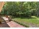 View of a spacious backyard with a wood deck, brick patio, and lush trees at 18 Red Pine Rd, Chapel Hill, NC 27516