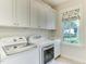 Well-lit laundry room with modern washer and dryer units, storage cabinets, sink, and window at 1830 Wilshire Ave, Raleigh, NC 27608