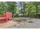 Landscaped backyard features a red deck, garden beds, brick pavers, and gravel, all surrounded by mature trees at 716 Beddingfield Dr, Knightdale, NC 27545