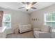 Well-lit bedroom with a crib, neutral walls, large windows, and a comfortable accent chair at 1304 Castlebay Rd, Durham, NC 27703