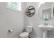 A well-lit half bath with a pedestal sink, round mirror, and a decorative wall shelf at 1304 Castlebay Rd, Durham, NC 27703