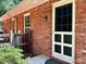 Close-up of a brick exterior with a white screen door, window, and green foliage at 207 Wood Cir, Chapel Hill, NC 27514