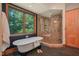 Modern bathroom with a luxurious soaking tub, brick shower, and large window offering scenic views at 3707 Stonegate Dr, Chapel Hill, NC 27516