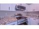 Close-up of the kitchen featuring stainless steel oven, microwave, granite countertops, and white cabinets at 4928 Silverdene St, Raleigh, NC 27616