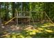 A wooden playground set with a slide and swing is situated in a backyard surrounded by trees at 102 Bluegrass Dr, Oxford, NC 27565