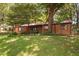 Cozy brick ranch-style home with a lush green lawn and mature trees providing shade and curb appeal at 1120 E Oak Dr, Durham, NC 27712