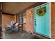 Inviting covered porch with seating area, brick facade, and a cheerful turquoise front door with wreath at 1120 E Oak Dr, Durham, NC 27712