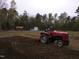Red Mahindra tractor tilling the soil in the backyard, showcasing a rural lifestyle property at 4008 Old Nc 86, Hillsborough, NC 27278