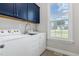 Bright laundry room with blue cabinets, stainless steel sink and window with a view at 119 Florentino Ct, Clayton, NC 27527