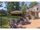 Inviting patio with stone accents, comfortable seating, and a charming outdoor fireplace beneath a tan umbrella at 2012 Silverleaf Dr, Youngsville, NC 27596