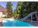Backyard pool with slide surrounded by mature landscaping and lush green trees under a bright blue sky at 2012 Silverleaf Dr, Youngsville, NC 27596
