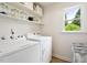 Bright laundry room with a window, modern washer and dryer, and open shelving for storage at 5833 Dahlberg Dr, Raleigh, NC 27603