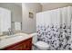 Bathroom with granite sink, cherry wood cabinet, toilet, and shower with flower-themed curtain at 8101 Claybrooke Ct, Willow Springs, NC 27592