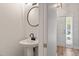 A well-lit powder room with a pedestal sink and round mirror adjacent to a doorway to the entry at 3021 Winding Waters Way, Raleigh, NC 27614