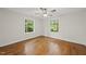Empty bedroom with hardwood floors, a ceiling fan, and two windows offering a serene view of the trees outside at 4301 Azalea Dr, Raleigh, NC 27612