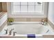 Bathroom with a deep soaking tub, neutral tile surround, and a bright, frosted window at 418 Magna Dr, Durham, NC 27703