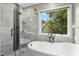 Bright bathroom features a glass shower and soaking tub near a window overlooking lush greenery at 5301 Denmead Way, Raleigh, NC 27613