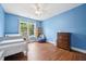Comfortable bedroom with blue walls, wood floors, ceiling fan, and bright window at 1818 Misty Hollow Ln, Apex, NC 27502