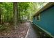 View of the side of the blue home, framed by lush greenery and gravel path at 9709 Greenfield Rd, Chapel Hill, NC 27516