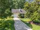 Front exterior featuring a driveway leading up to a charming yellow home, lush green lawn, and mature trees at 11901 N North Exeter Way Way, Raleigh, NC 27613