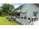 Back exterior view of the charming white farmhouse showcasing the deck, patio, and landscaped yard at 125 Attena Way, Zebulon, NC 27597