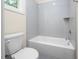 Bathroom with a white bathtub and shower combo with grey tiled walls, complemented by a toilet and window at 225 Whistlers Cv, Louisburg, NC 27549