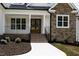 Front entrance featuring a brick staircase leading to a covered porch with a wooden front door and stone siding at 225 Whistlers Cv, Louisburg, NC 27549