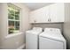 Bright laundry room with side-by-side washer and dryer, cabinet, and view to backyard through large window at 725 E Maple Ln, Fuquay Varina, NC 27526