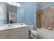 Bright bathroom featuring a vanity with sink, tiled shower-tub, toilet, blue walls, and large mirror at 3311 Canoe Brook Pkwy, Raleigh, NC 27614