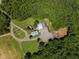 Aerial view showcases an estate with main house, garages, and outbuildings surrounded by a dense forest at 4050 Culbreth Rd, Stem, NC 27581