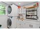 Laundry room showcases a stackable washer/dryer, wooden cabinets, open shelving, and a sink at 4404 Oak Park Rd, Raleigh, NC 27612