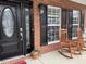 Covered front porch featuring a decorative black door, rocking chairs, and stylish black shutters at 1126 Woodlands Creek Way, Apex, NC 27502