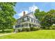 White two-story home featuring a welcoming front porch, black shutters, and green lawn with mature shade trees at 401 N Main St, Louisburg, NC 27549