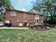 Brick exterior home featuring a wooden deck, lush green lawn, mature trees, and an outdoor generator at 105 Abbotsford Ct, Durham, NC 27712