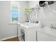 Well-lit laundry room with white washer, dryer, sink, wire shelving, and a window overlooking the yard at 25 Harlow Ct, Fuquay Varina, NC 27526