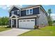 Side view of a navy two-story home featuring a two-car garage, neat landscaping and a blue sky at 3813 Rosebush Dr, Zebulon, NC 27597