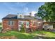 View of brick home's backyard featuring a well-manicured lawn, patio, and mature trees at 201 N Us 301, Micro, NC 27555